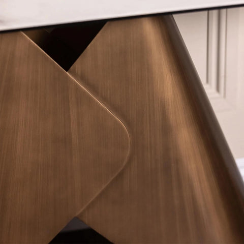 Close-up of a modern table leg with a brushed bronze metal finish, showing a curved corner detail and a white tabletop surface.