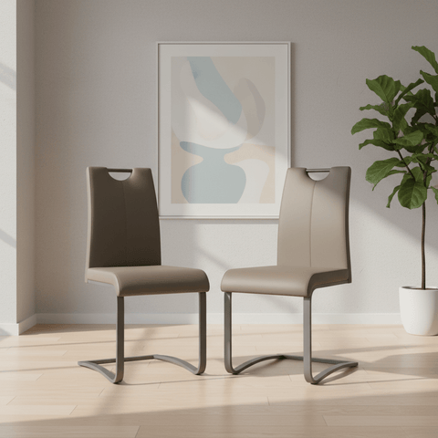 Two modern cantilever dining chairs with taupe upholstered seats and backs and curved metallic legs, shown in a bright, minimalist dining room setting with a framed abstract print and a potted plant.