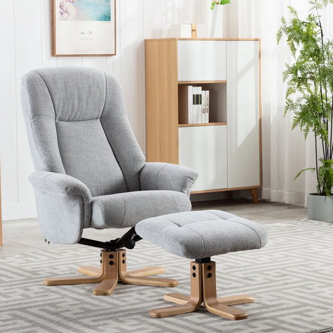 A light gray fabric bigelow recliner chair with a matching ottoman, both with wooden swivel bases, shown in a bright, modern living room setting.