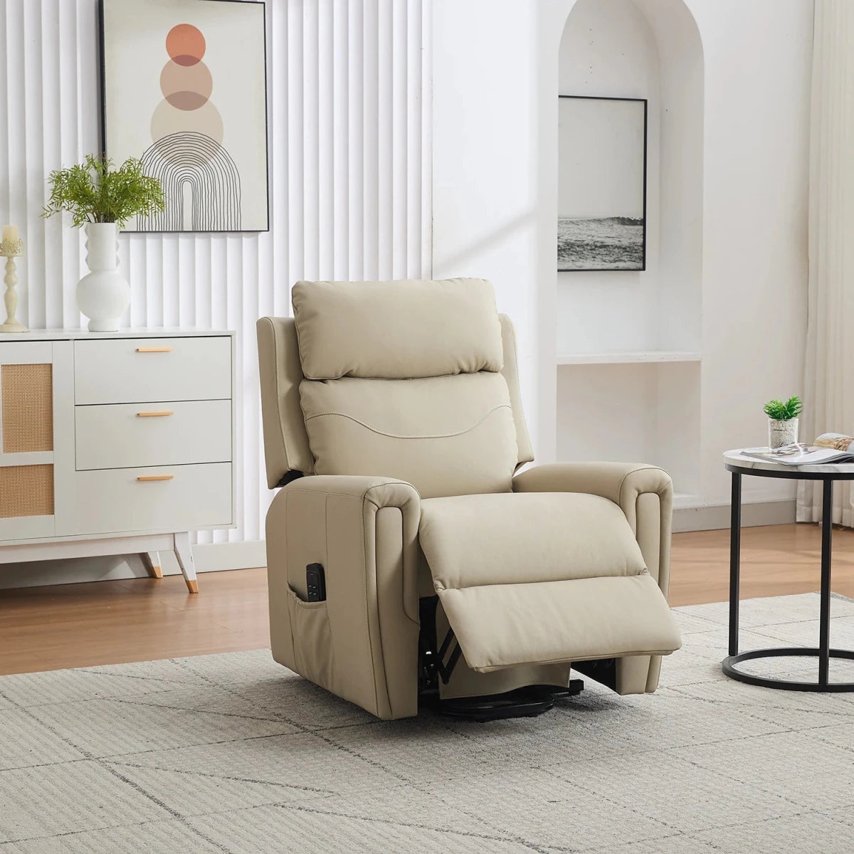 A beige leather riser  recliner chair with the footrest extended, set in a modern, bright living room with a white sideboard, framed art, and a small round side table.