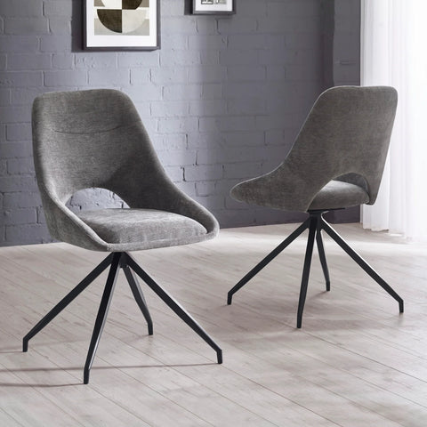 Two gray upholstered chairs with black metal legs on a light wooden floor against a gray brick wall.