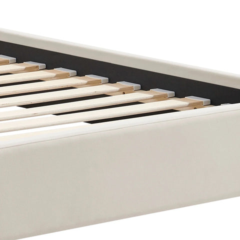 Close-up of a bed frame corner showing a light beige velvet upholstered foot end and natural wood slats.