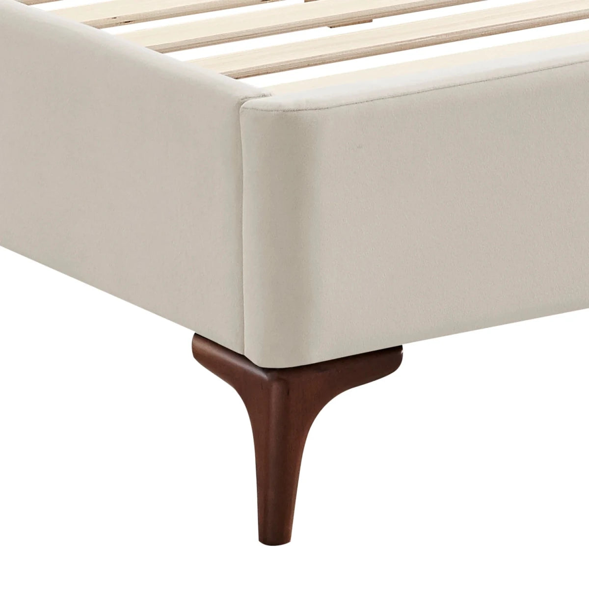 Camila Luxury Bed - Close-up of a bed frame corner with a cream upholstered headboard or side panel, light wood slats, and a dark brown wooden leg.