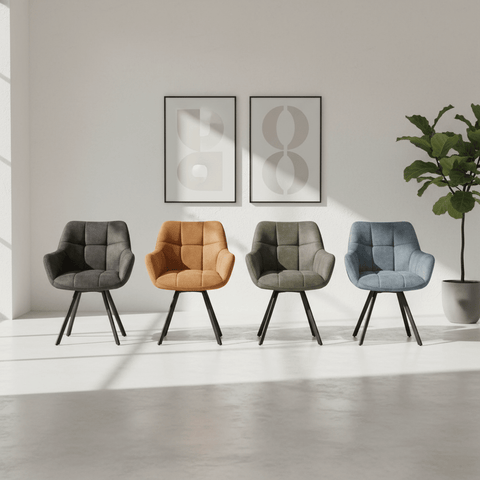 Four upholstered Dining chairs in dark gray, camel, sage green, and light blue, arranged in a row on a light gray floor against a white wall with framed art and a potted plant.