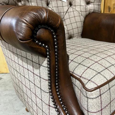 Close-up of a brown leather armrest with decorative nailhead trim on a plaid sofa.