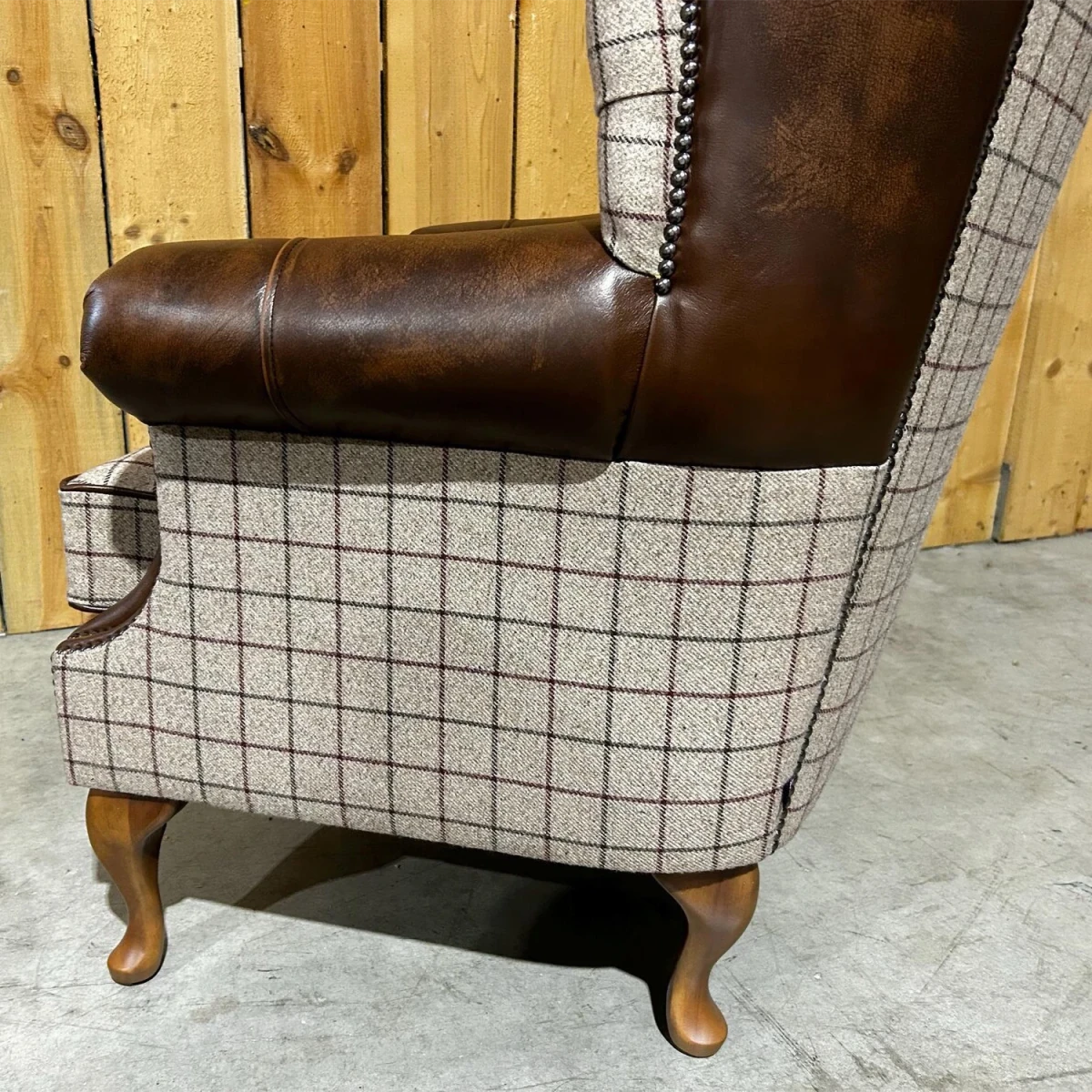 Chair with brown leather armrests and plaid fabric backrest against a wooden panel background