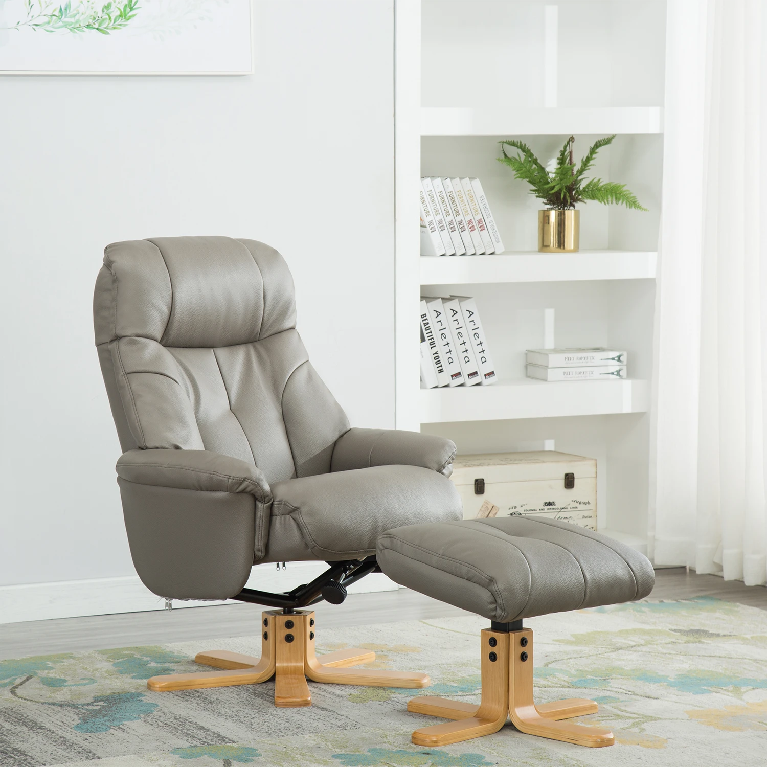 A taupe gray faux leather recliner chair with a matching ottoman, set in a bright, modern room with a white bookshelf in the background.
