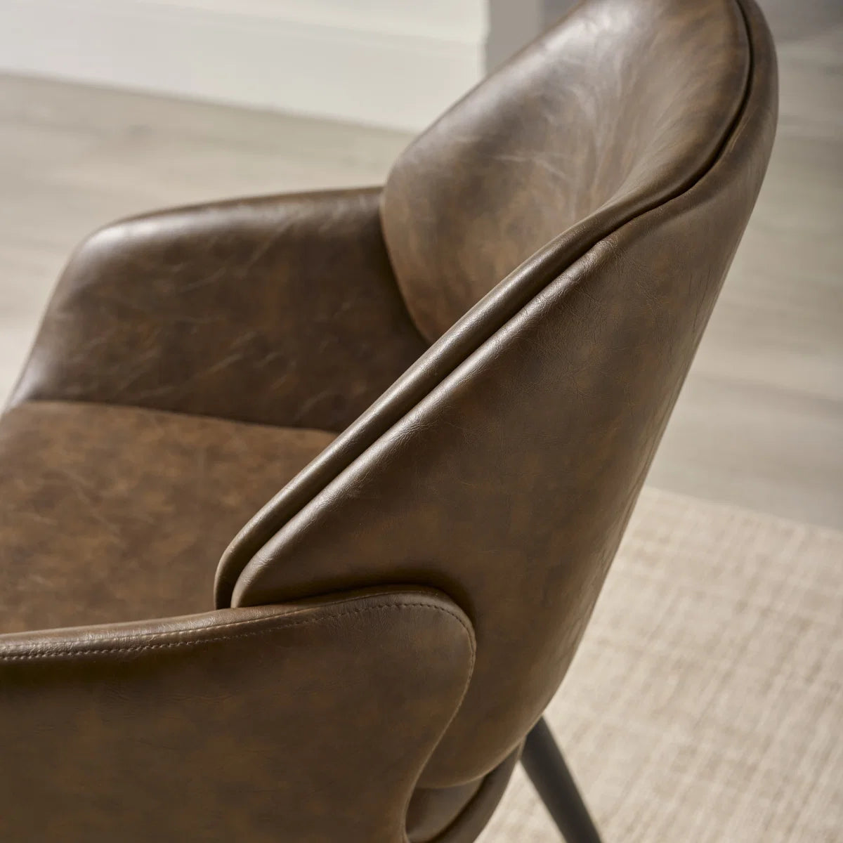 Chair close up of Parker Brown Faux Leather Dining Chairs with padded seats, curved armrests and black metal legs 