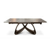 A modern rectangular dining table with a dark wood grain top and a sculptural, interlocking curved metal base in a dark bronze finish, shown on a white background.