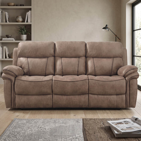 A three-seat reclining sofa upholstered in taupe-brown plush fabric, shown in a staged living room setting with a rug, bookshelf, lamp, and window.