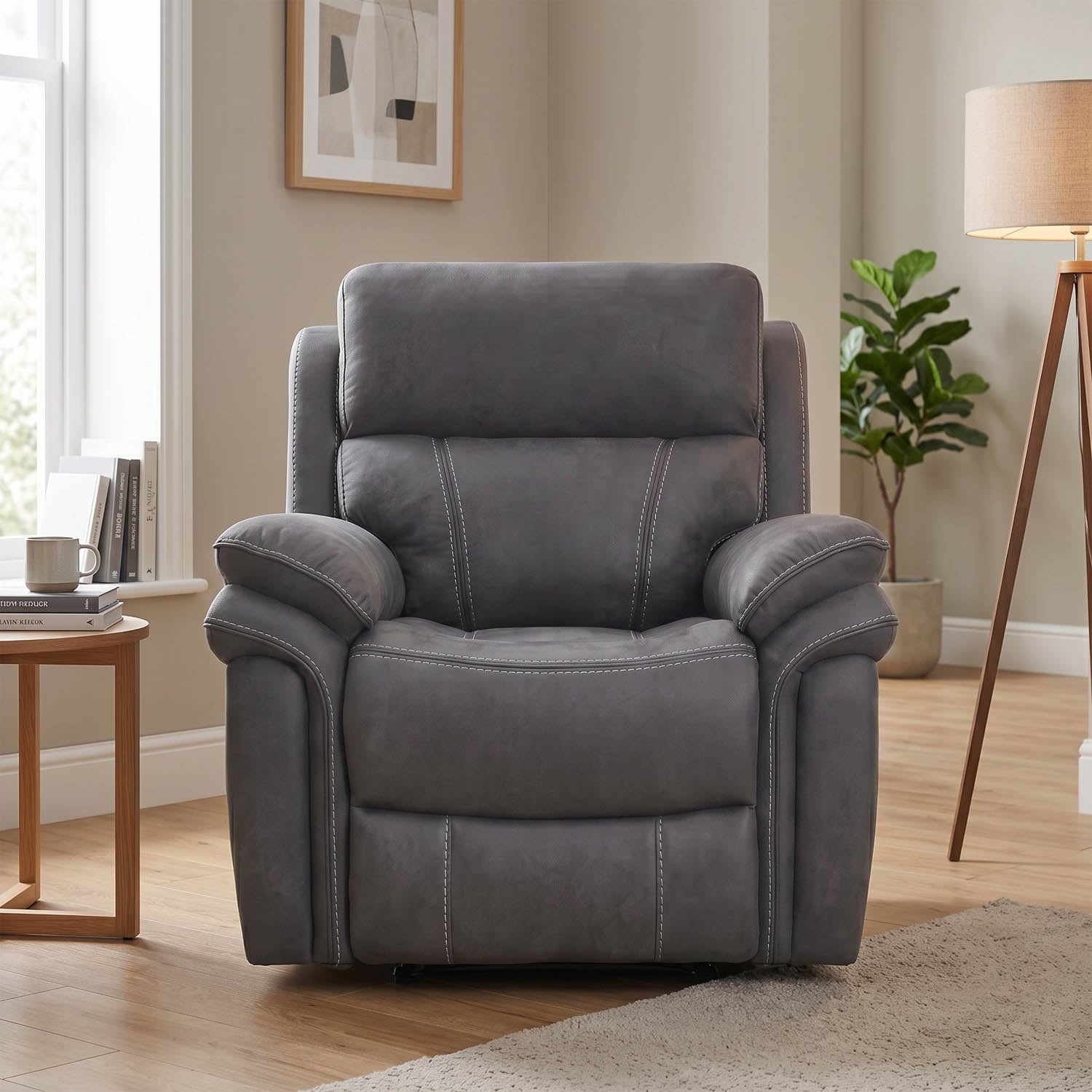 A gray upholstered recliner chair with visible contrast stitching, shown in a styled living room setting with a side table, window, plant, lamp, and wood floor.