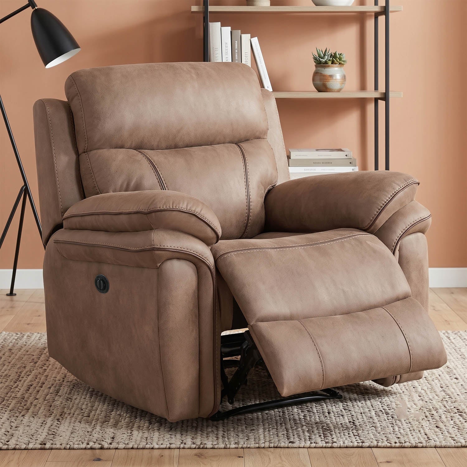 A brown faux-leather recliner chair with the footrest extended, set in a living room environment with a bookshelf, floor lamp, and patterned rug.