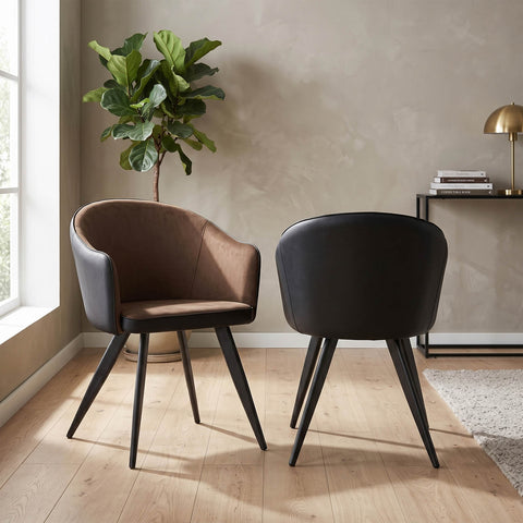 Two modern bucket-style dining chairs with tapered black metal legs, shown in a styled room setting. One chair features a dark brown leather seat and back, while the other has a black leather seat and back.