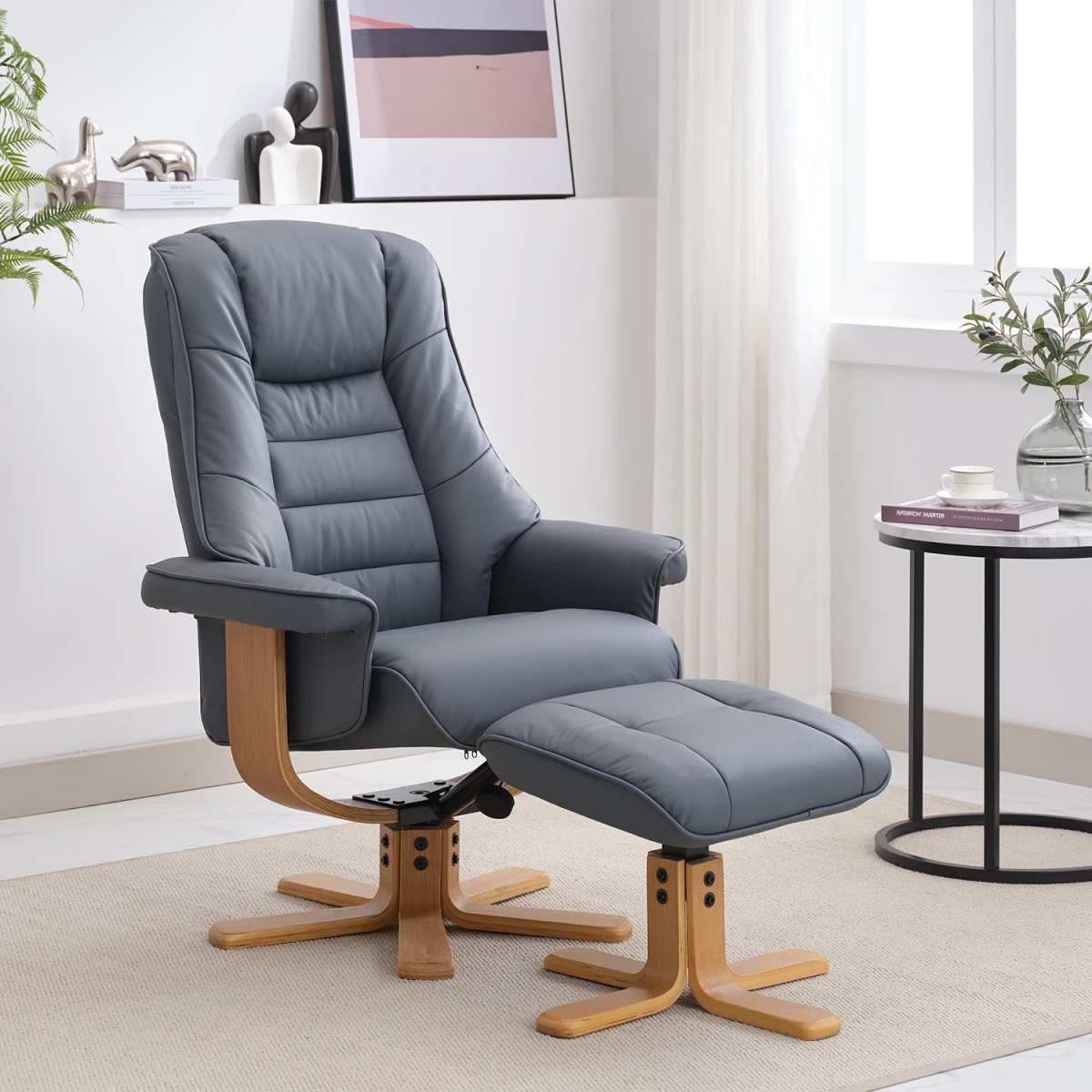 A gray upholstered recliner chair with a matching ottoman, shown in a styled living room setting with a side table, curtains, and framed wall art.