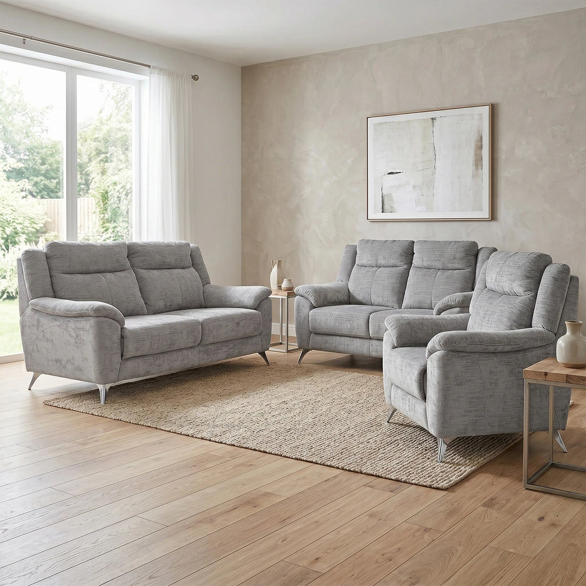 A light gray three-piece living room furniture set consisting of a loveseat, a recliner, and a sofa, arranged on a textured beige area rug in a modern living room with light wood floors and neutral walls.