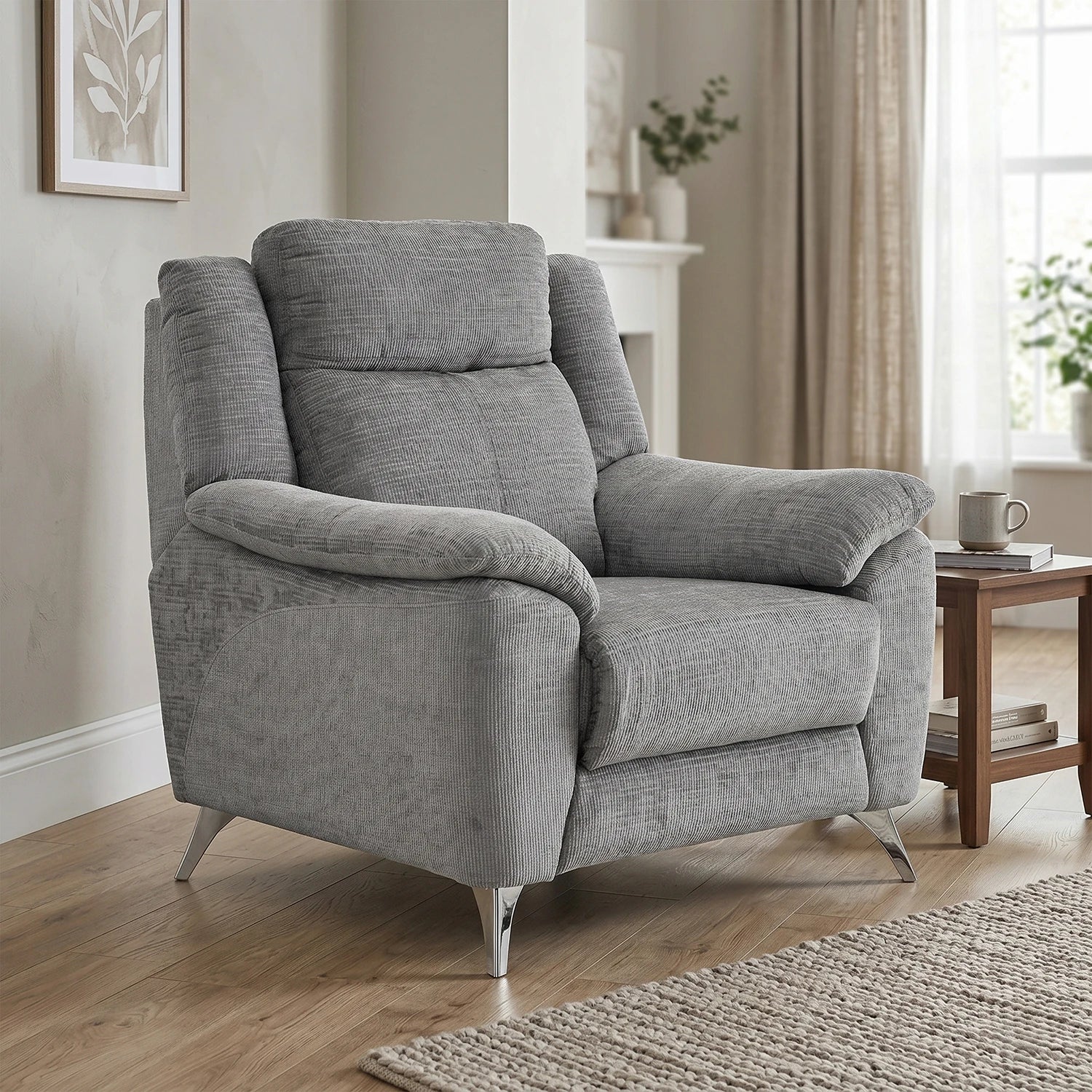 A light gray upholstered chair with rolled arms and tapered metal legs, shown in a styled living room setting with a side table, window, curtains, and wood flooring.