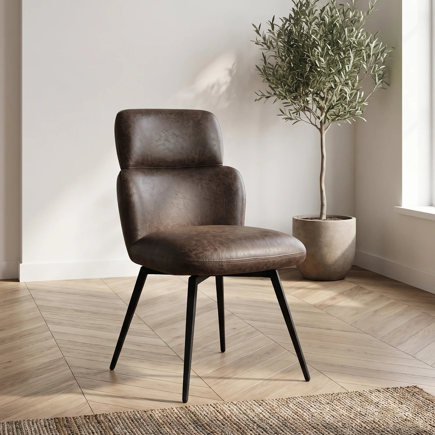 A dark brown faux vintage leather dining chair with black metal legs, positioned in a bright room with a light wood herringbone floor, a potted olive tree, and a woven rug.