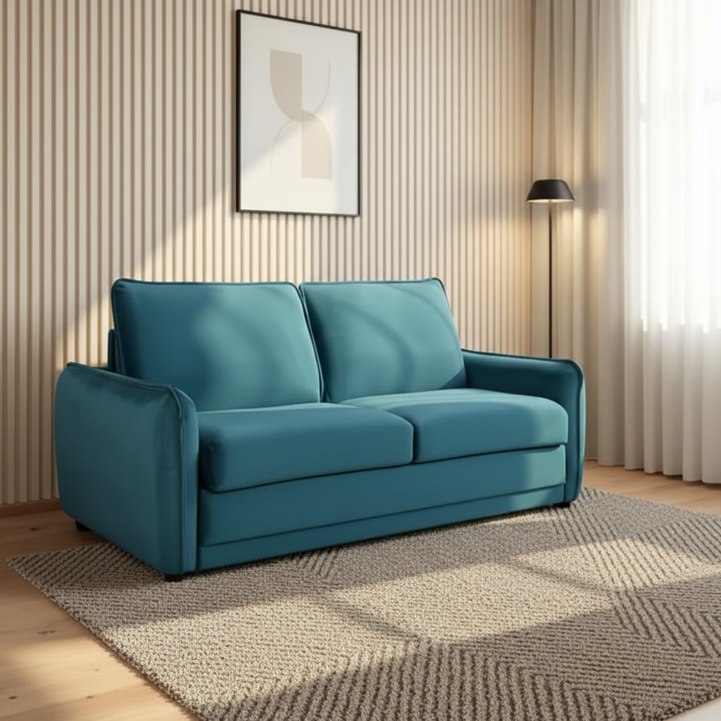 A teal blue upholstered loveseat sofa bed placed in a modern living room with a striped beige wall, framed abstract art, a floor lamp, white curtains, and a textured rug.
