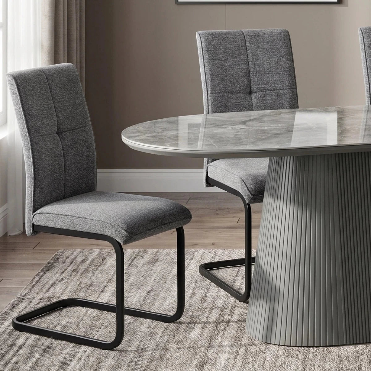 Venezia Dark gray upholstered dining chairs with black cantilever black metal base beside a round marble-top dining table in a modern room setting.