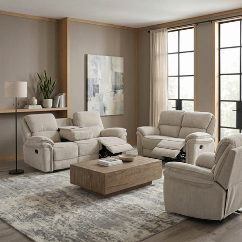 A staged living room showing a coordinated set of upholstered seating pieces: a reclining loveseat, a matching reclining armchair, and a separate reclining chair, arranged around a wood coffee table on a patterned rug. The room has beige walls, wood trim, large windows with sheer drapes, and wall art.