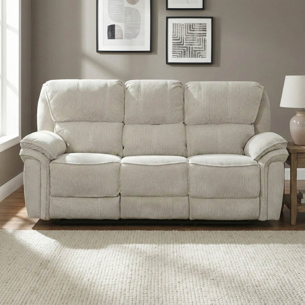 Beige recliner 3 seater sofa in a living room with framed art on the wall.